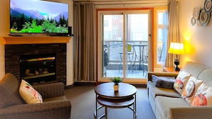 Een woonkamer met een open haard, een televisie, een bank, een salontafel en een balkon met tuinmeubilair.