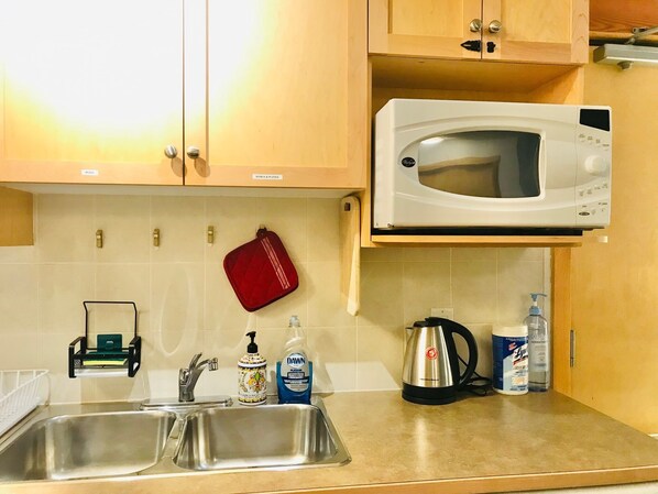 A kitchen with a stainless steel sink, a microwave, a kettle, and various kitchen items on the counter.
