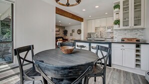A modern kitchen with white cabinetry, a central island, and a dining area with a round table and chairs. - Luxurious Lakefront Haven - Prime Ski Access & Majestic Mountain Views! (Dillon)