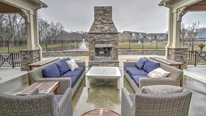 An outdoor patio with wicker furniture, a stone fireplace, and a view of houses in the background. - 4 Mi to Bethany Beach: Townhome w/ Screened Porch (Millville)