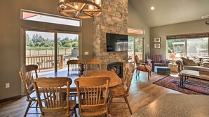 A spacious living room with a stone fireplace, a dining area with wooden chairs, a large flat-screen TV, and a cozy seating area with a sofa and armchairs. - Rustic Cabin Near Mt Rainier: Fire Pit & BBQ! (Packwood)