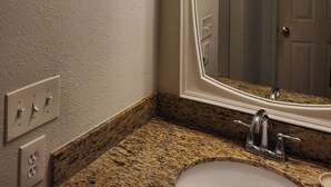 Un baño con un espejo grande, encimera de granito y un aplique en la pared.