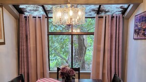 Un comedor con una mesa, sillas, un jarrón con flores y vista a árboles por una ventana.