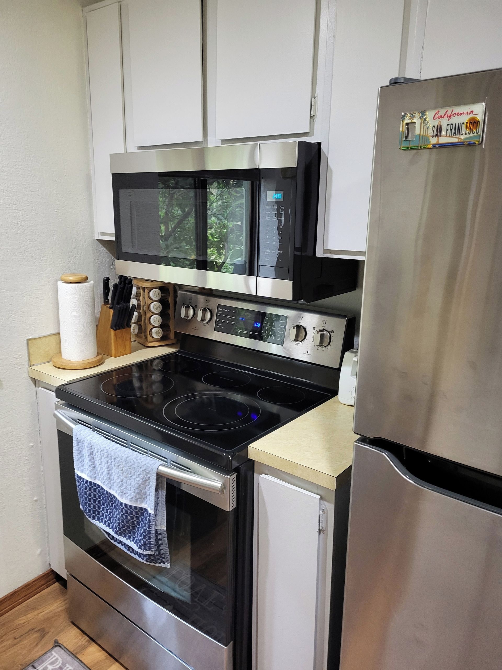 A compact kitchen with a stainless steel refrigerator, a microwave, an oven, and a stovetop.
