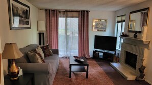Una sala de estar con un sofá, una mesa de centro, un televisor de pantalla plana, una chimenea y un ventanal con cortinas.