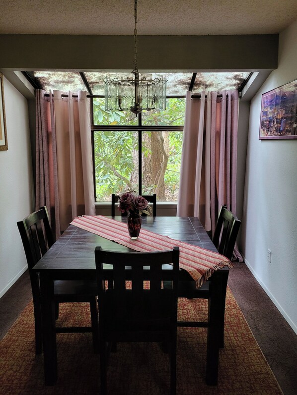 A dining area with a table, chairs, a vase with flowers, and a view through a window.