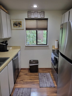 A compact kitchen with a window, a trash bin, and a refrigerator.