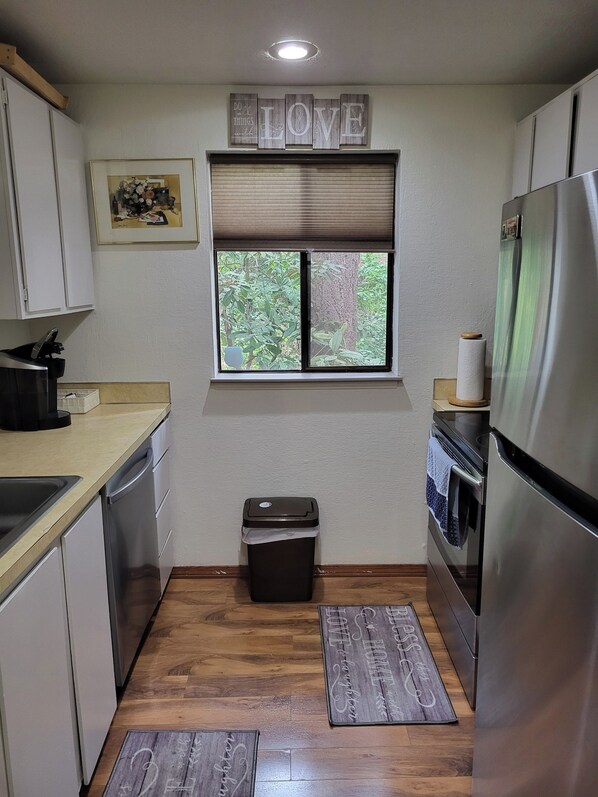 A compact kitchen with a window, a trash bin, and a refrigerator.