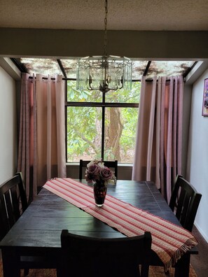 A dining area with a table, chairs, a vase with flowers, and a window with curtains.