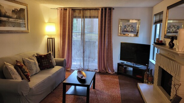 Una sala de estar con sofá, mesa de centro, televisor de pantalla plana, chimenea y ventana con cortinas.