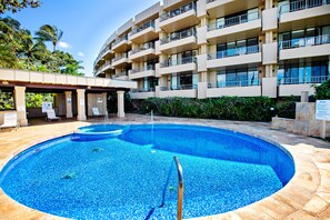 Une piscine de forme circulaire, entourée d’un bâtiment doté de nombreux balcons et d’un espace couvert avec des chaises.