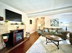 A living room with a fireplace, sofa, coffee table, and a flat-screen TV mounted on the wall.