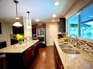 A modern kitchen with granite countertops, stainless steel appliances, and a large window offering a view.