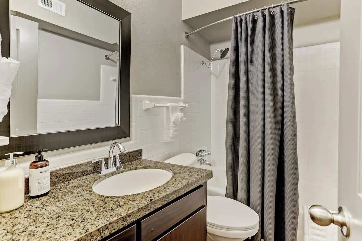 A bathroom with a granite countertop sink, a mirror, a toilet, and a shower curtain.