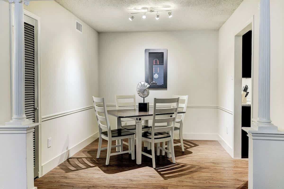 A dining area with a round table and six chairs, a decorative vase, and a framed picture on the wall.