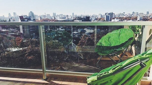 Un balcón con vistas a un paisaje urbano, una silla verde y un bolso verde.