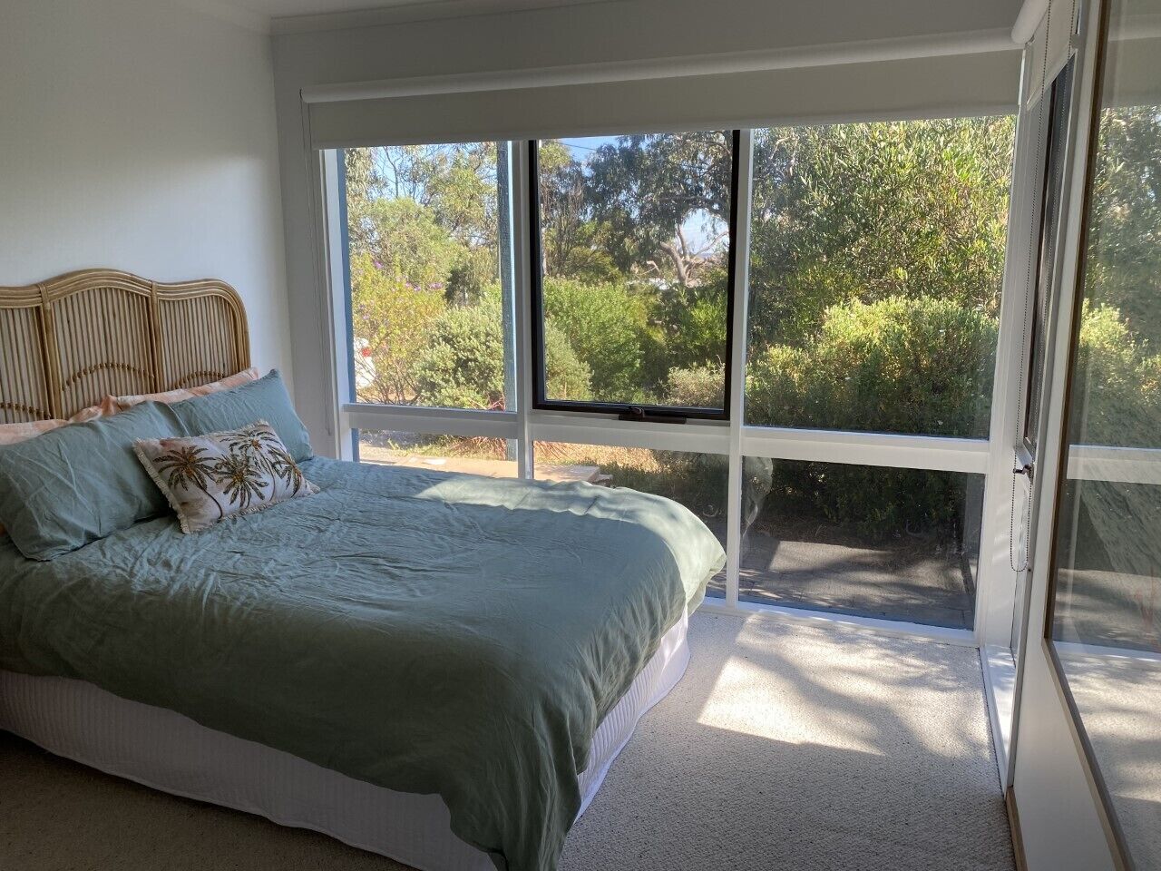 A bedroom with a large window, a bed with a green bedspread, and a wooden headboard.