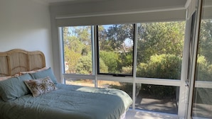 A bedroom with a large window, a bed with a green bedspread, and a wooden headboard. - BEAUTIFUL BEACH HOUSE - BRILLIANT POSITION (Anglesea)