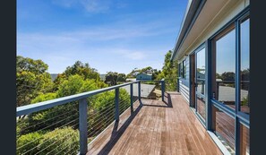 A wooden deck with a metal railing, large windows, and a view of greenery and a distant building. - BEAUTIFUL BEACH HOUSE - BRILLIANT POSITION (Anglesea)