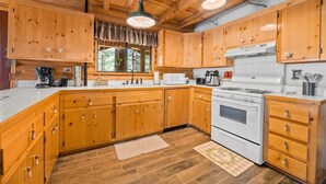 A wooden cabin-style kitchen with a large stove, wooden cabinets, and a window with curtains.