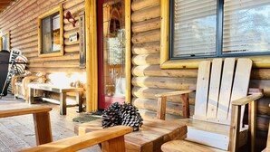 A log cabin with a wooden porch, a red door, and a welcome sign.