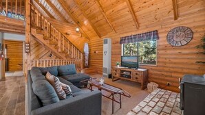 A wooden cabin interior with a sofa, TV, and a stone-patterned rug.