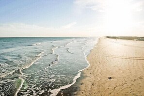 A beach with waves reaching the shore, a clear sky, and a sandy path leading along the water. - Gorgeous water front home with amazing views and fishing! (Sargent, TX)