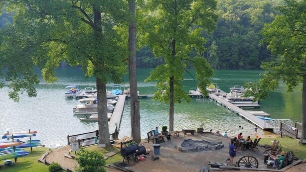 A lakeside patio with a barbecue area, picnic tables, and a dock with boats. - Family-Friendly, Private 2 Acres with Stunning Views (Topton)