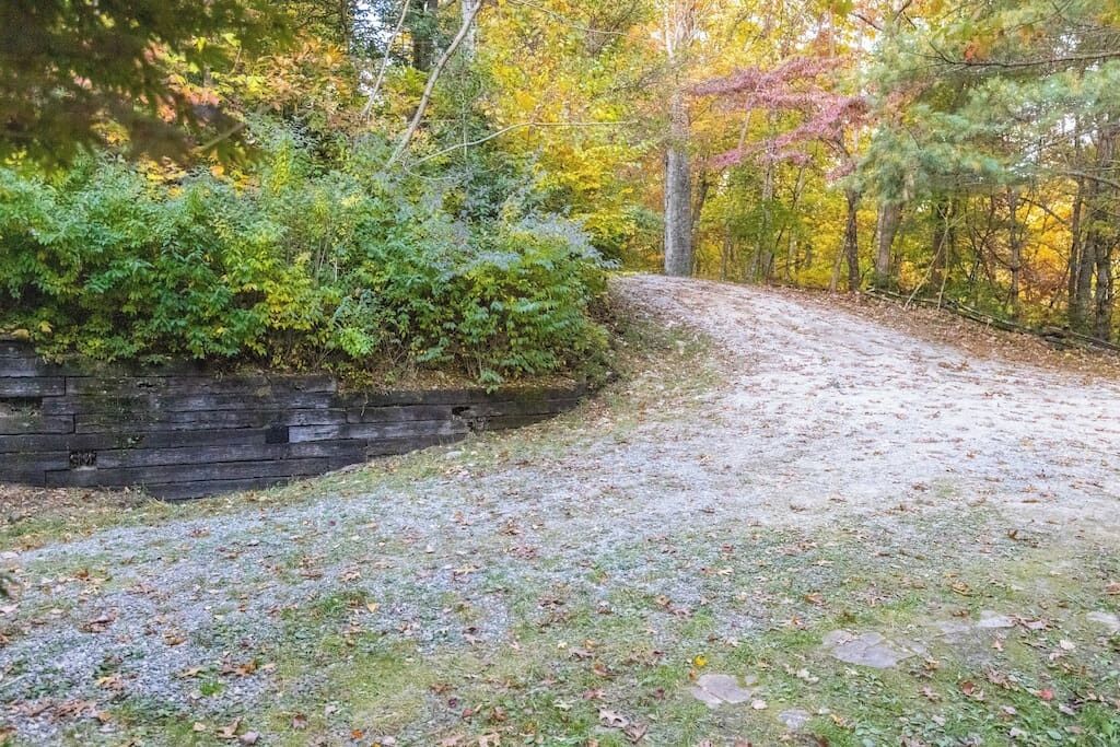 A gravel path leading through a wooded area with dense foliage and a stone wall on one side.