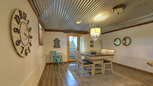 Uma sala de jantar com mesa de madeira, cadeiras, um candelabro e um relógio de parede grande.