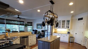 A modern kitchen with a central island, white cabinetry, stainless steel appliances, and a hanging pot rack. - Live in a mansion near the city, offering a resort-style setup. (Duluth)