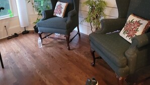 A room with two dark green armchairs, a wooden floor, a framed floral painting on the wall, and a window with a view of greenery. - Live in a mansion near the city, offering a resort-style setup. (Duluth)