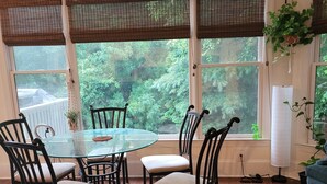 A dining area with a round glass table surrounded by four chairs, large windows with blinds, a ceiling fan, and a view of greenery outside. - Live in a mansion near the city, offering a resort-style setup. (Duluth)