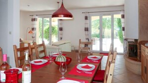 Een eetgedeelte met een lange houten tafel, gedekt voor een maaltijd, rode placemats en een rode hanglamp.