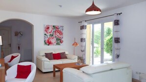 Een moderne woonkamer met een witte bank, een rode fauteuil, een houten salontafel en een bloemschilderij aan de muur.