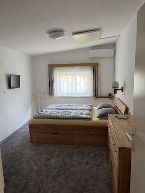 A bedroom with a bed, a dresser, a TV, and a window with curtains.