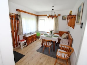 A cozy dining area with a wooden table set for four, surrounded by wooden chairs. A green ottoman and a wooden bench with cushions are also visible.
