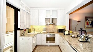 A compact kitchen with white cabinets, a stainless steel stove, a microwave, and a blender.