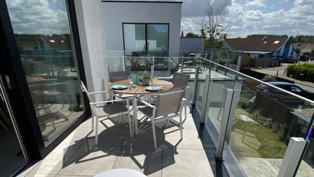 Een modern balkon met glazen hekwerk, een tafel met stoelen en uitzicht op de omgeving.
