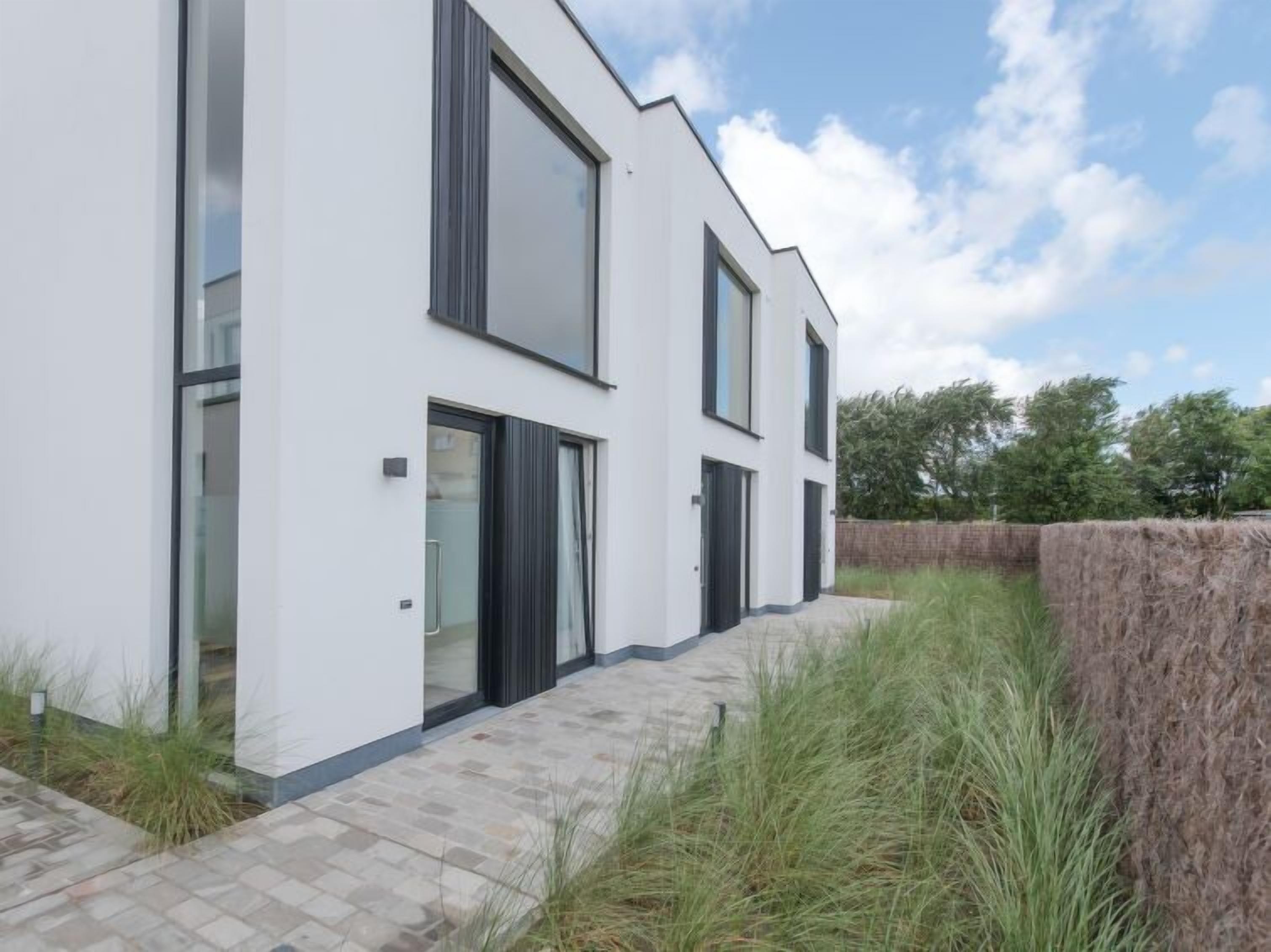 Une maison moderne à deux étages, dotée de grandes fenêtres et d’une allée pavée menant à l’entrée.