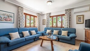 A living room with a blue sectional sofa, a wooden coffee table, and large windows with curtains. - Pintor Beach House by Interhome (Port Pollença)