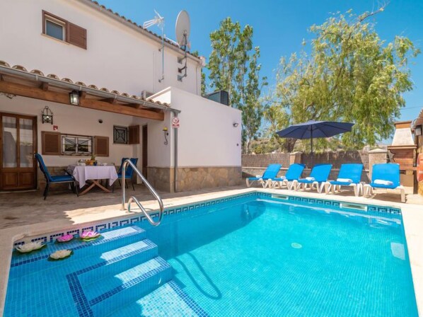 Una piscina amb rajoles blaves, una para-sol i gandules.
