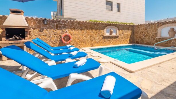 A pool area with blue lounge chairs, a barbecue grill, and a stone wall. - Pintor Beach House by Interhome (Port Pollença)