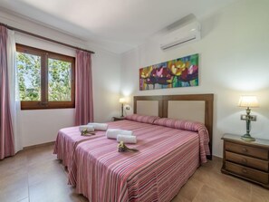Una habitació d'hotel amb un llit gran, dues taules de nit, una finestra amb cortines, un quadre a la paret i un aparell d'aire condicionat.