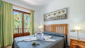 A hotel room with a bed, two bedside lamps, a wooden nightstand, a painting on the wall, and a balcony with curtains. - Pintor Beach House by Interhome (Port Pollença)