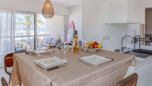 A dining area with a table set for two, a surfboard, and a fruit bowl. - La Rose des Sables by Interhome (Saint Cyr sur mer Les Lecques)