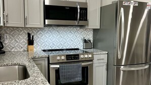 A modern kitchen with white cabinets, a stainless steel refrigerator, a microwave, an oven, and a granite countertop. - GOTL Strip Suite #2- Sunset Vacation Rentals (Geneva)