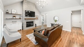 A spacious living room with a stone fireplace, a leather sofa, a striped armchair, and a wooden coffee table. - Executive Stay, Modern Farmhouse Perfect Location. Garage Parking. (Broken Arrow)