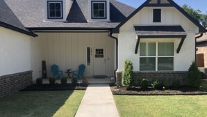 A two-story house with a front porch, a mailbox, and a small garden with shrubs and a lawn. - Executive Stay, Modern Farmhouse Perfect Location. Garage Parking. (Broken Arrow)