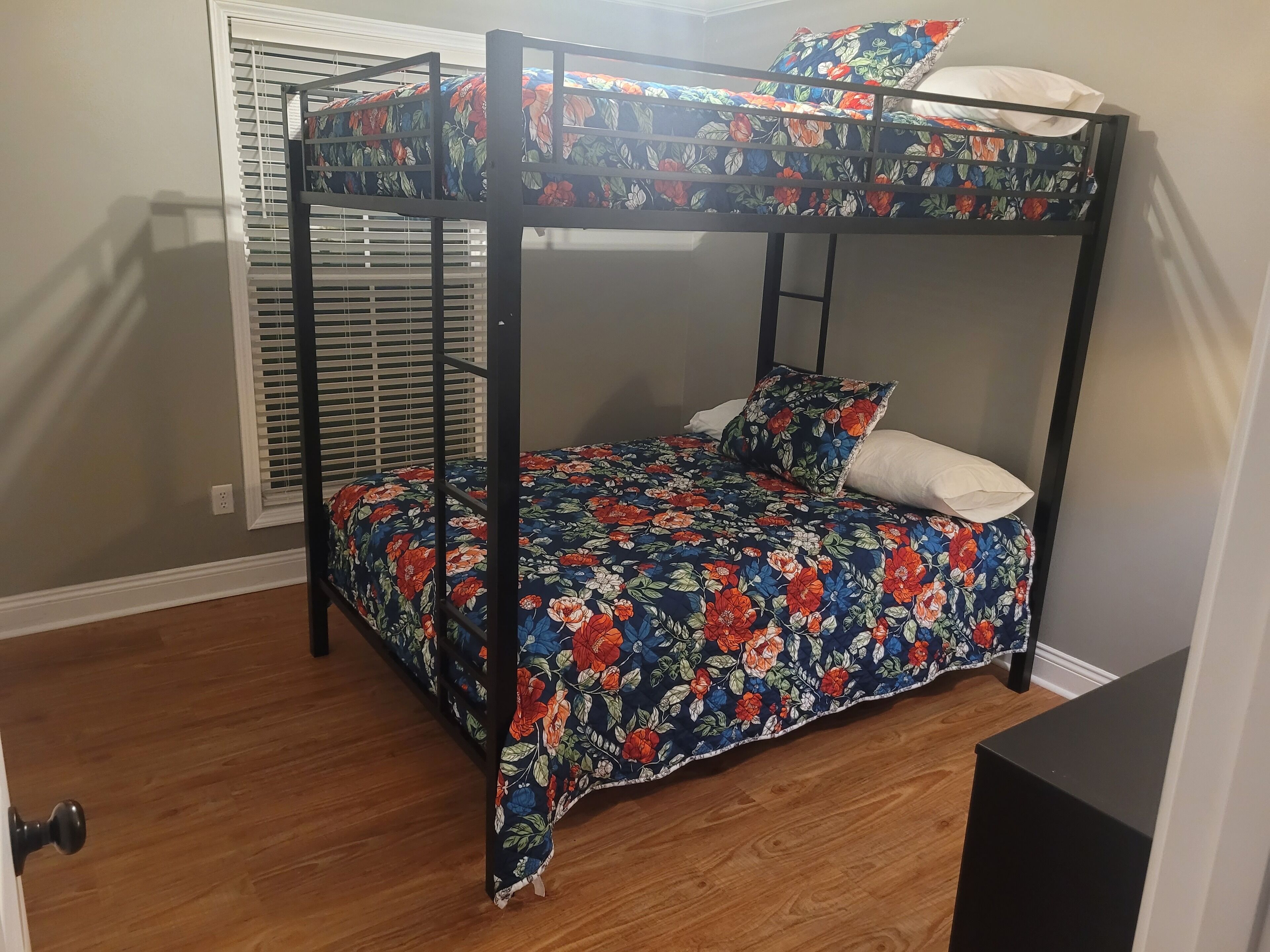 A bunk bed with floral bedding, a window with blinds, and a wooden floor.